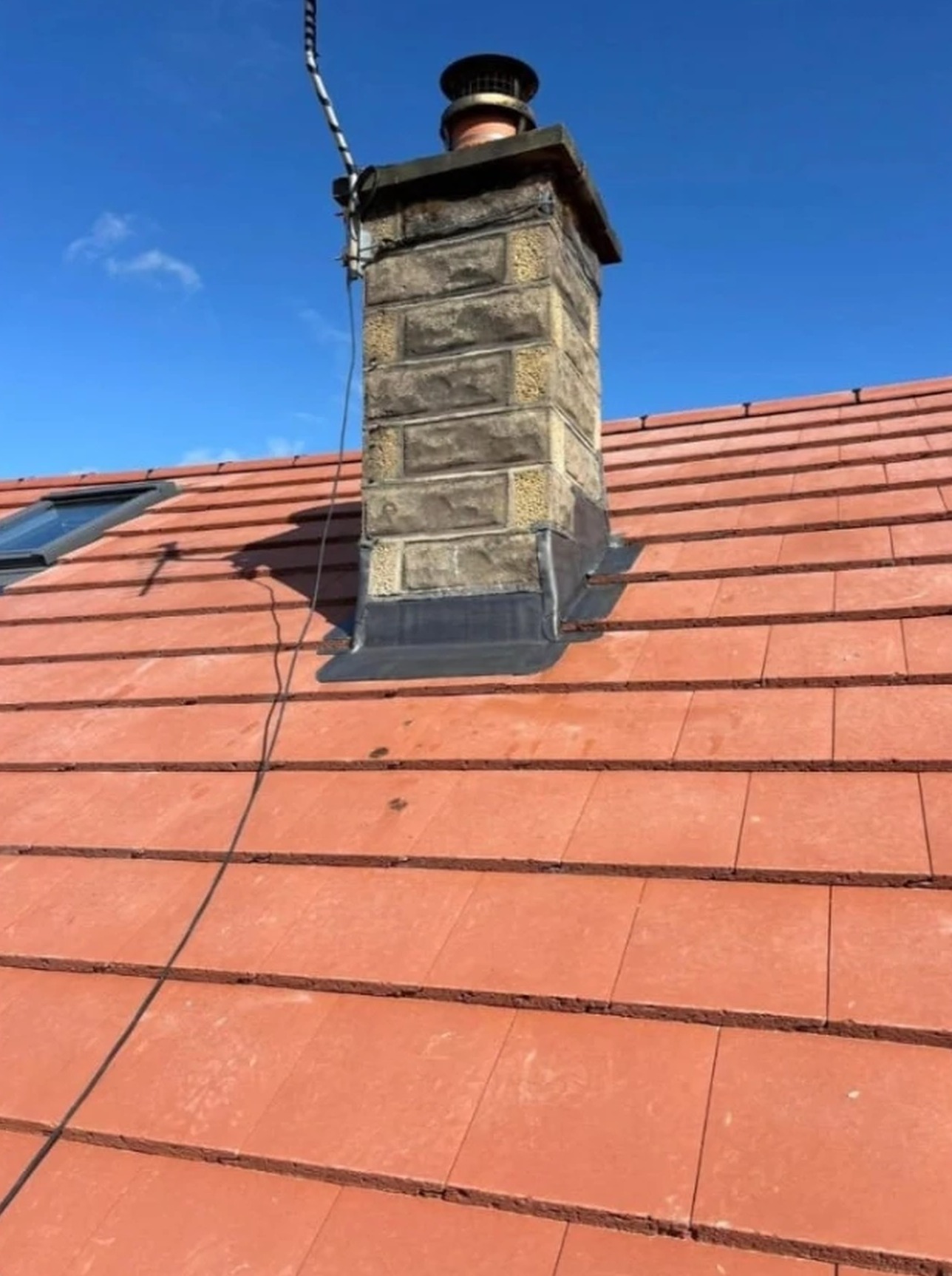 Repointed stone chimney stack with new lead flashing on a red tiled roof